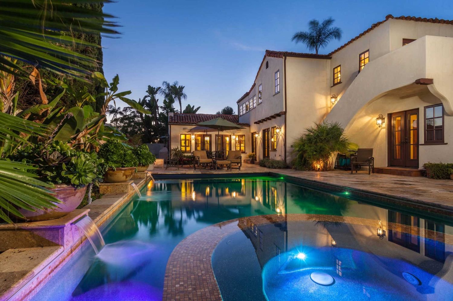 Warm exterior and pool lighting around a home at dusk