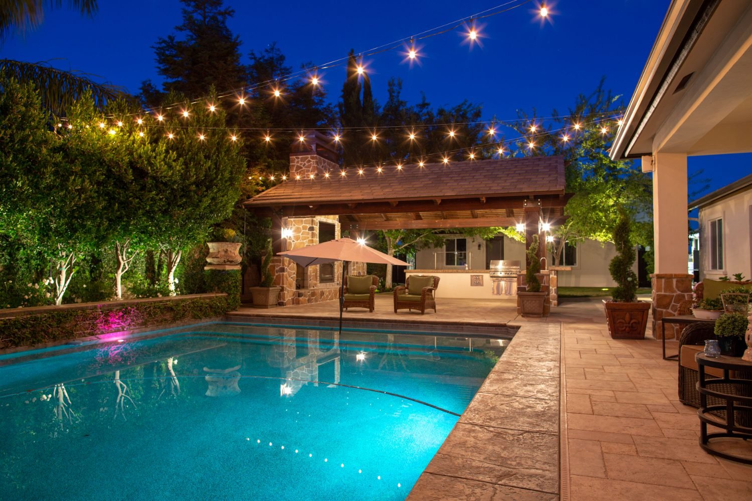 String lights glowing over a poolside pergola and outdoor kitchen in Bakersfield