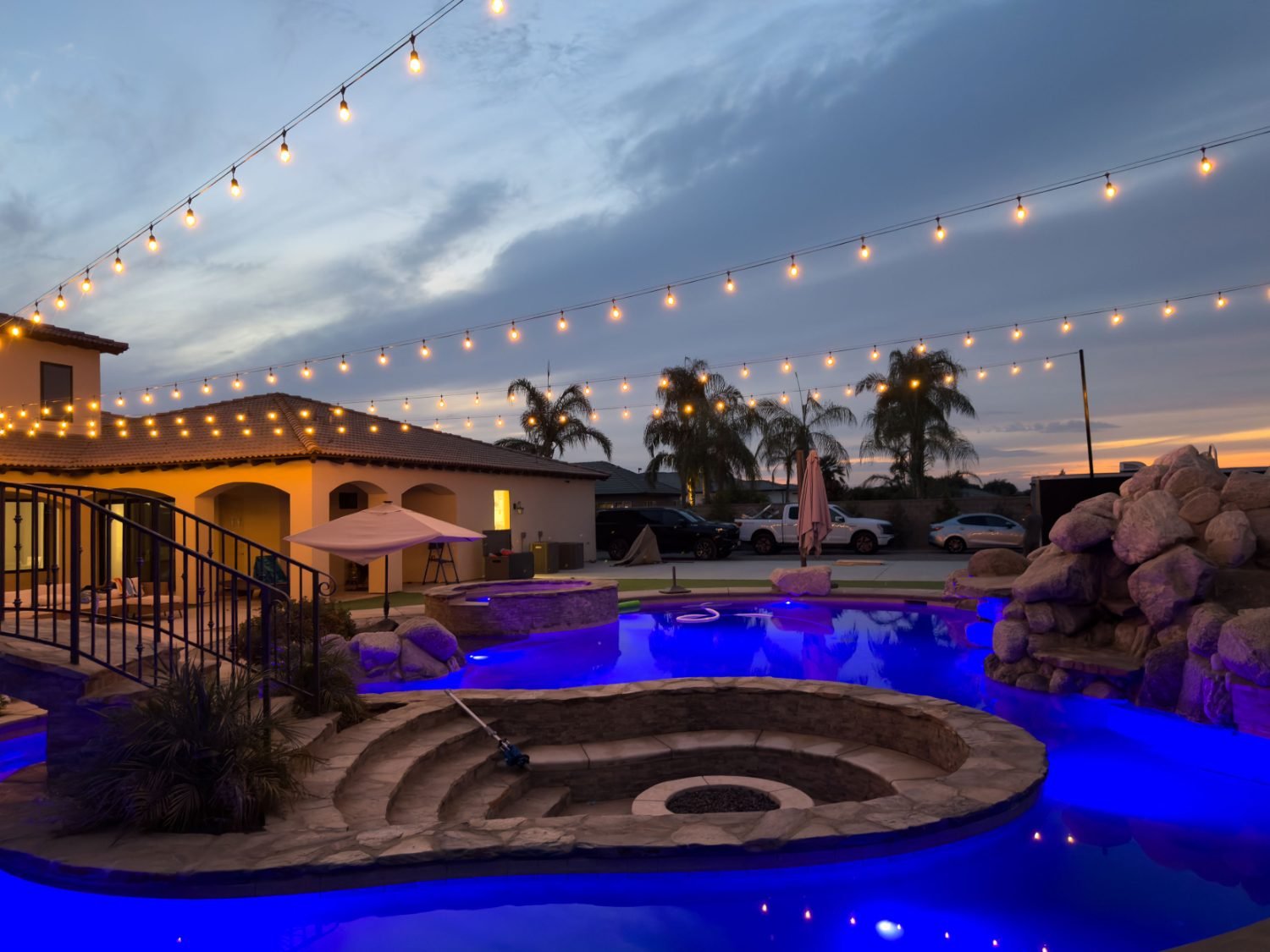 Bistro string lights over a resort-style Bakersfield pool with a lit rock waterfall and spa